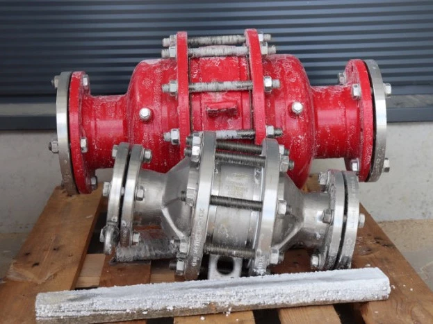 Two industrial inline safety devices or flame arresters, one red and one silver, resting on a wooden pallet with visible frost residue in an outdoor setting.