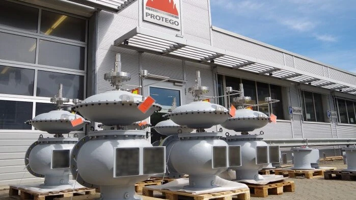 Several large gray industrial valve units sit on wooden pallets outside a PROTEGO facility under a blue sky.