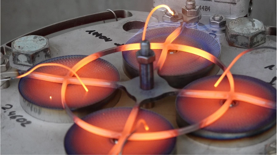 Glowing gas burner flames forming circular patterns on an industrial metal surface, illustrating high-temperature heating technology.