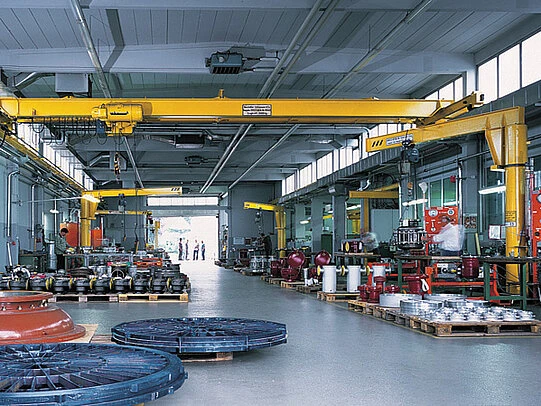 Large industrial workshop with overhead cranes and metal components arranged on pallets.