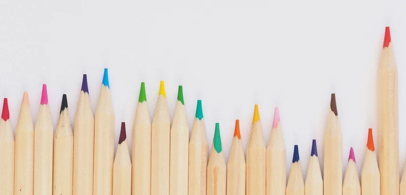 Une rangée de crayons de couleur bien taillés longe le bord inférieur d'un fond blanc, laissant un espace vide au-dessus.