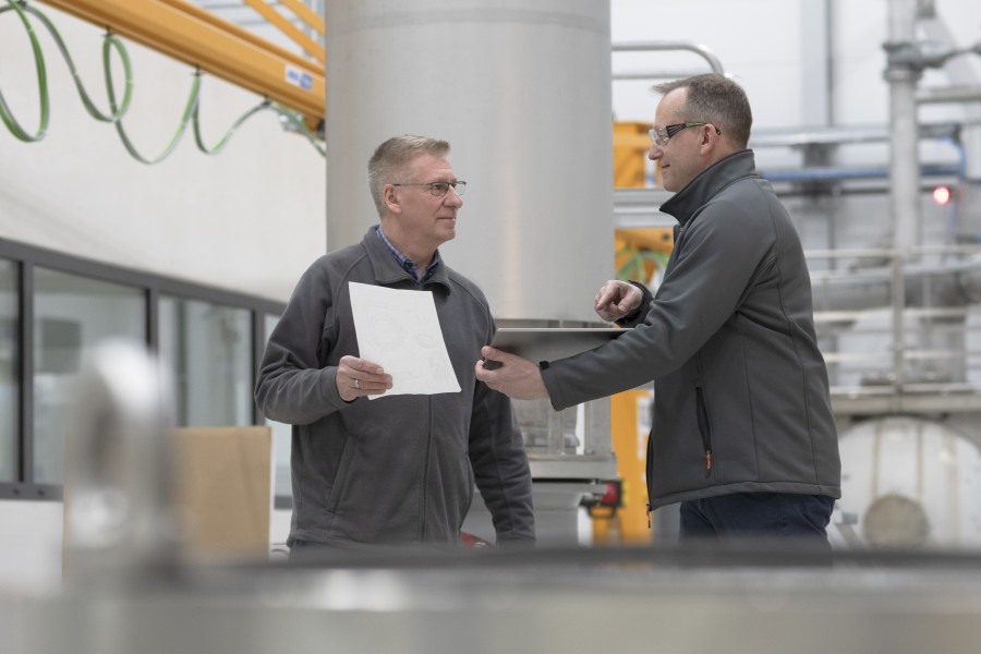 A supervisor discussing a document with an employee in an industrial setting, showcasing expertise at a glance for glossary purposes