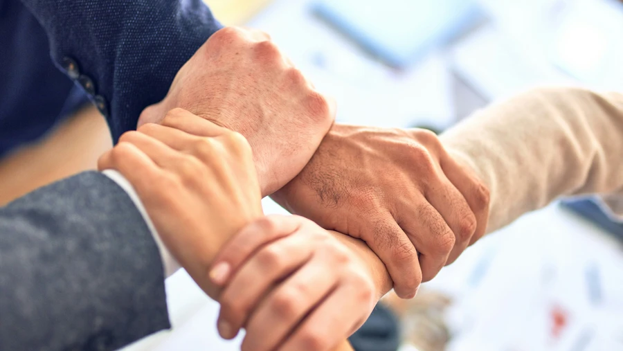 Four hands gripping each other's wrists, symbolizing teamwork, unity, and collaboration in a professional setting.