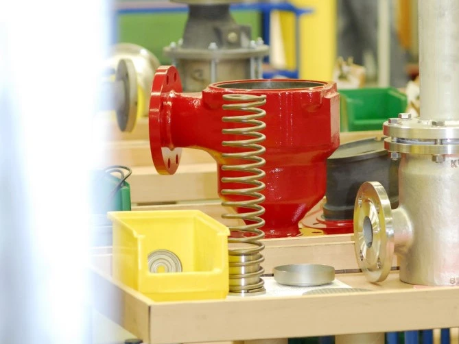 A red industrial valve housing with a large metal spring and various mechanical parts laid out on a workbench.