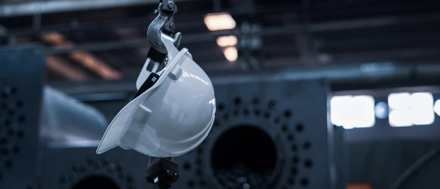 White safety helmet hanging in an industrial setting, representing HSE and quality standards
