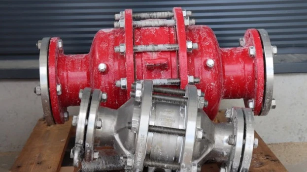 Two industrial inline safety devices or flame arresters, one red and one silver, resting on a wooden pallet with visible frost residue in an outdoor setting.