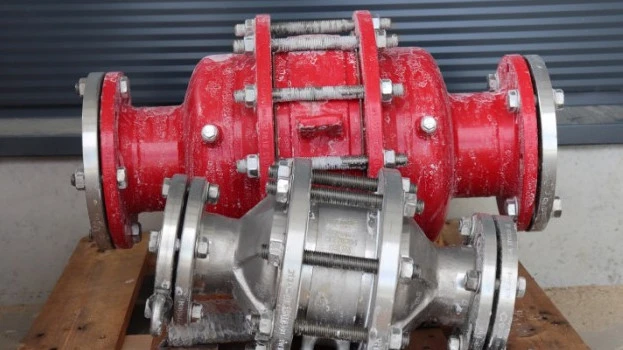 Two industrial inline safety devices or flame arresters, one red and one silver, resting on a wooden pallet with visible frost residue in an outdoor setting.