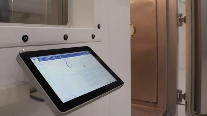 Touchscreen control panel mounted beside a sealed industrial test chamber door inside a laboratory or processing facility.