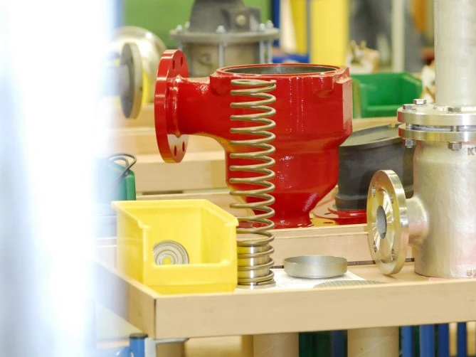 A red industrial valve housing with a large metal spring and various mechanical parts laid out on a workbench.
