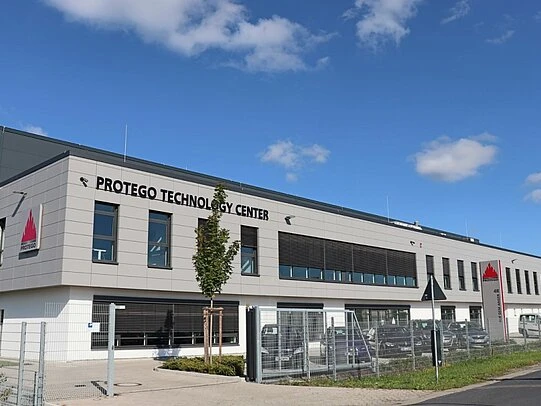 Exterior view of the Protego Technology Center, a modern industrial office building with signage, fenced parking, and a blue sky overhead.