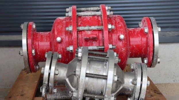 Two industrial inline safety devices or flame arresters, one red and one silver, resting on a wooden pallet with visible frost residue in an outdoor setting.
