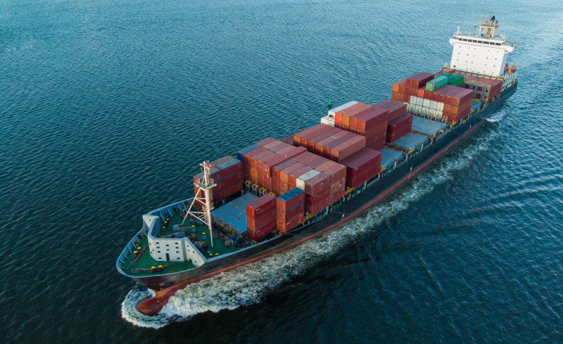 A cargo ship loaded with containers sailing through the ocean, representing marine and offshore industries