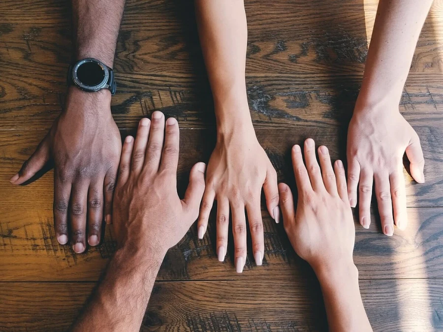 Hands of different people laid flat on a wooden table, representing unity and compliance