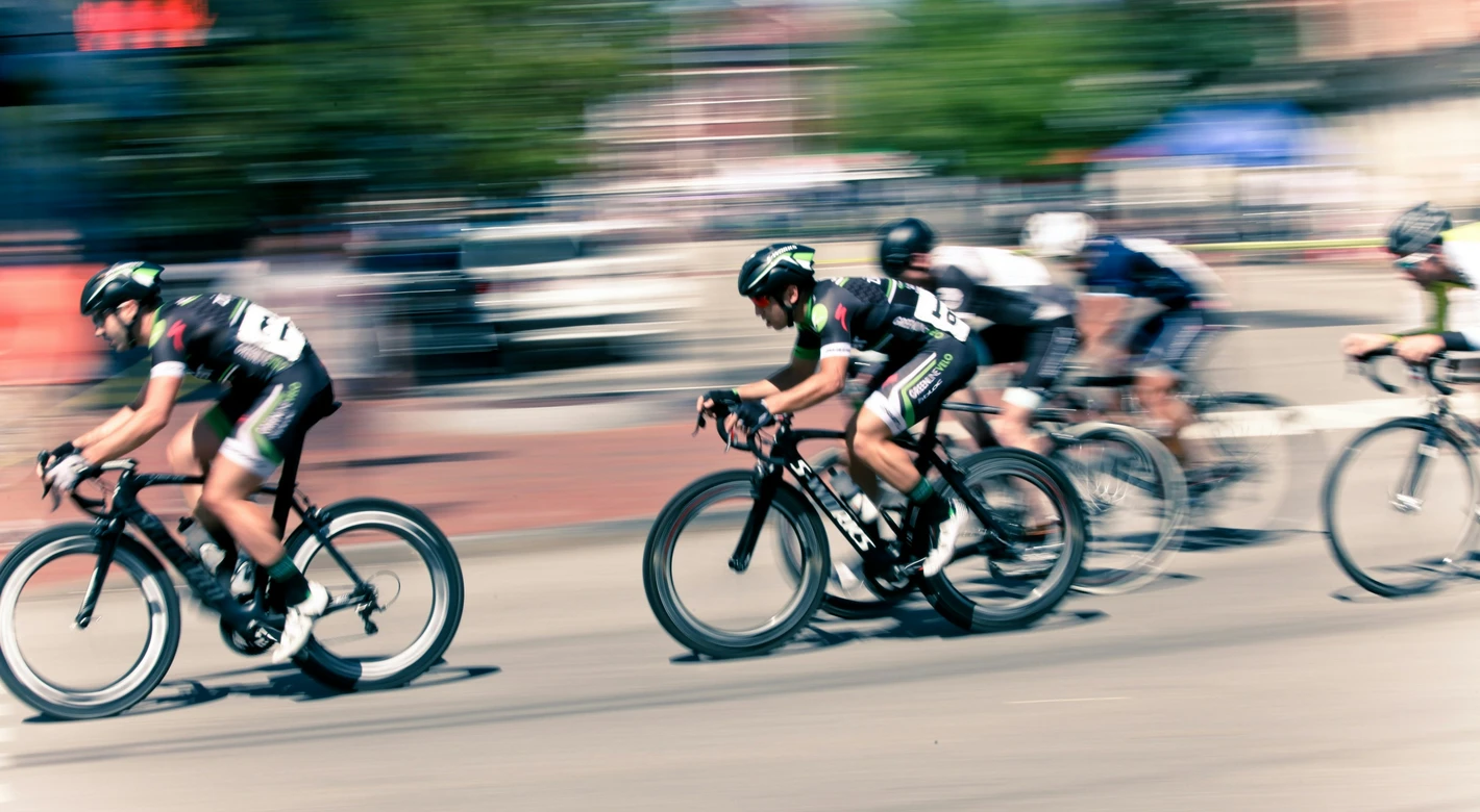 A pack of road cyclists races past with strong motion blur, emphasizing speed on a city street.