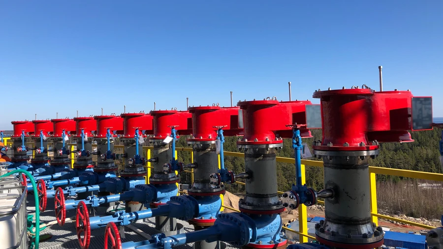 A row of large red industrial vent valves sits atop blue piping and handwheels on an outdoor platform under a clear blue sky.