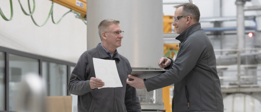 A supervisor discussing a document with an employee in an industrial setting, promoting compliance, respect, and tolerance