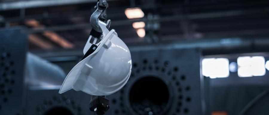 White safety helmet hanging in an industrial setting, representing HSE and quality standards