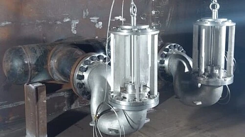 Two stainless steel valve assemblies are mounted on large industrial piping inside a metal-lined chamber.