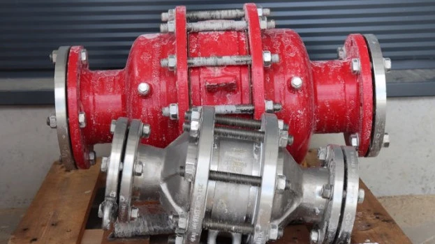 Two industrial inline safety devices or flame arresters, one red and one silver, resting on a wooden pallet with visible frost residue in an outdoor setting.