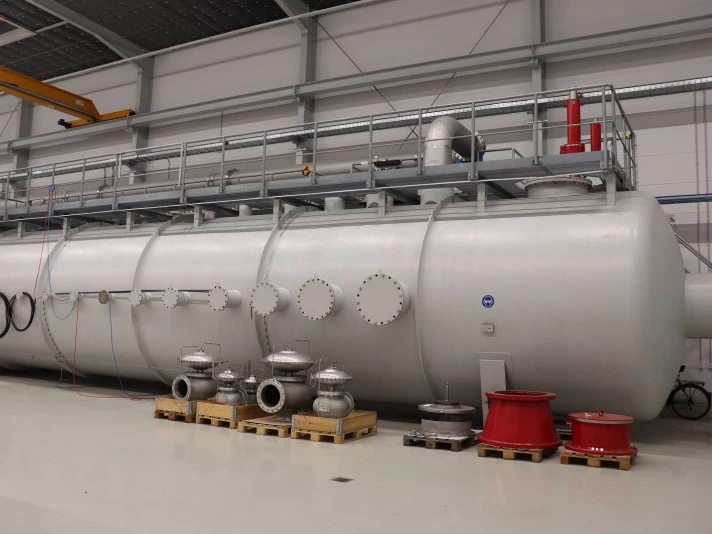 Großer horizontaler Industrie-Druckbehälter in einer Fabrikhalle, ausgestattet mit mehreren Flanschstutzen, Ventilen auf Paletten und einer erhöhten Wartungsplattform.