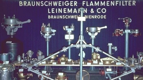 A display of industrial flame arresters and valves arranged on a table in front of a banner reading “Braunschweiger Flammenfilter Leinemann & Co.”
