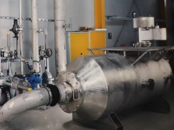 Industrielle Rohrleitungsinstallation mit einem großen zylindrischen Inline-Gerät, das mit Ventilen und Instrumenten innerhalb einer Verarbeitungs- oder Testanlage verbunden ist.