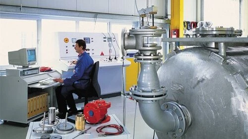 A technician monitors a large industrial piping system with a control workstation inside a test facility.