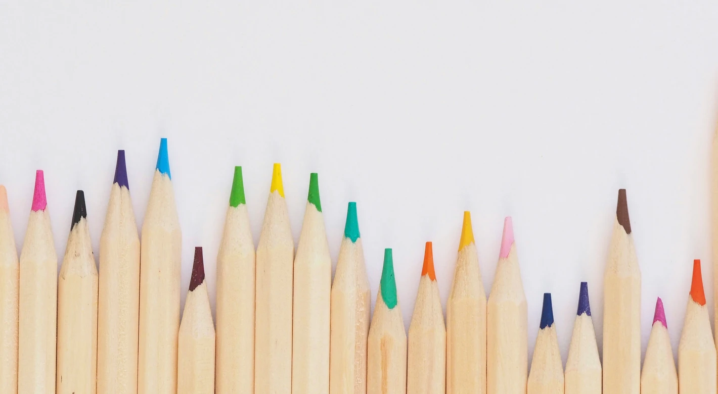 Una fila de lápices de colores afilados bordea el borde inferior de un fondo blanco, dejando un espacio en blanco en la parte superior.
