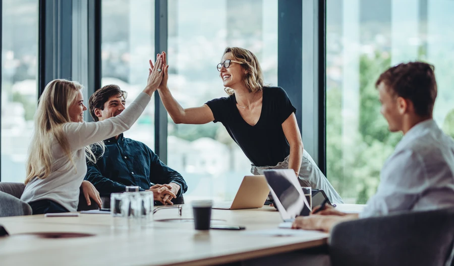 Dans un studio de design au style rétro, plusieurs personnes sont debout devant des tables à dessin inclinées et travaillent sur de grands plans techniques sous la lumière tamisée de la pièce.