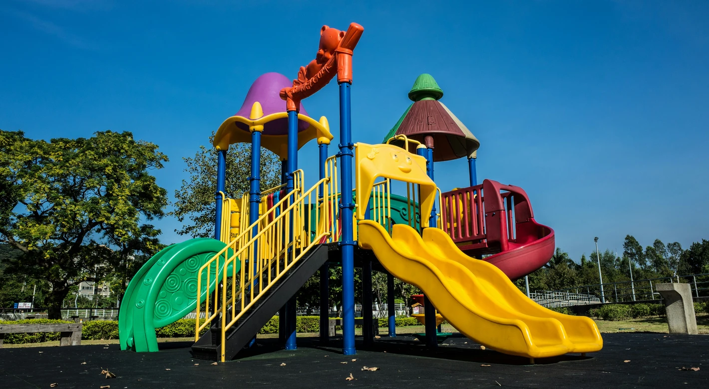 Una colorida estructura de parque infantil con toboganes y plataformas para trepar se alza bajo un cielo azul y despejado.