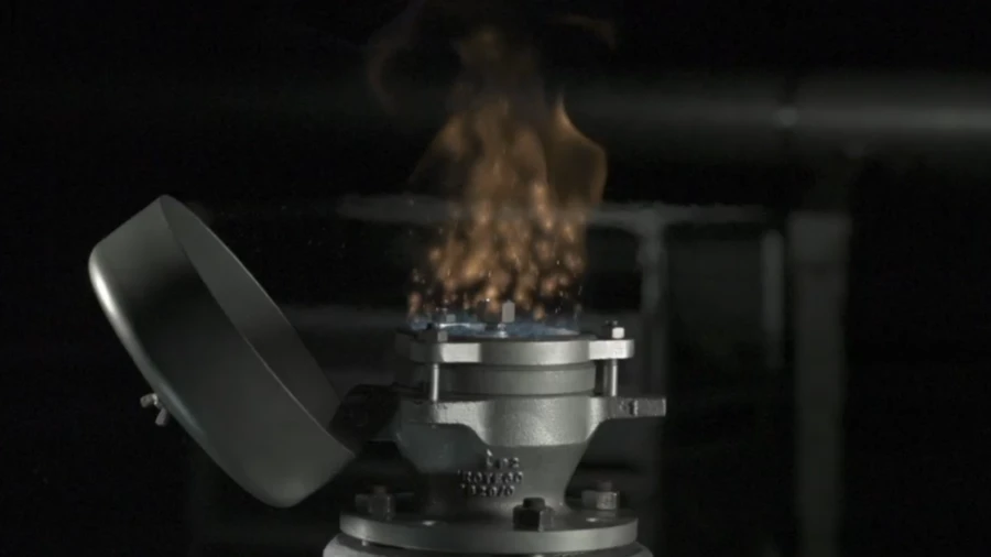 Close-up of an industrial flame arrester or valve emitting a controlled flame plume from its top during a dark, controlled ignition test.