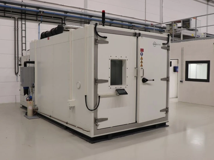 Große geschlossene industrielle Testkammer mit verstärkten Türen, Sichtfenster und Warnschildern, installiert in einer sauberen Fabrikhalle.
