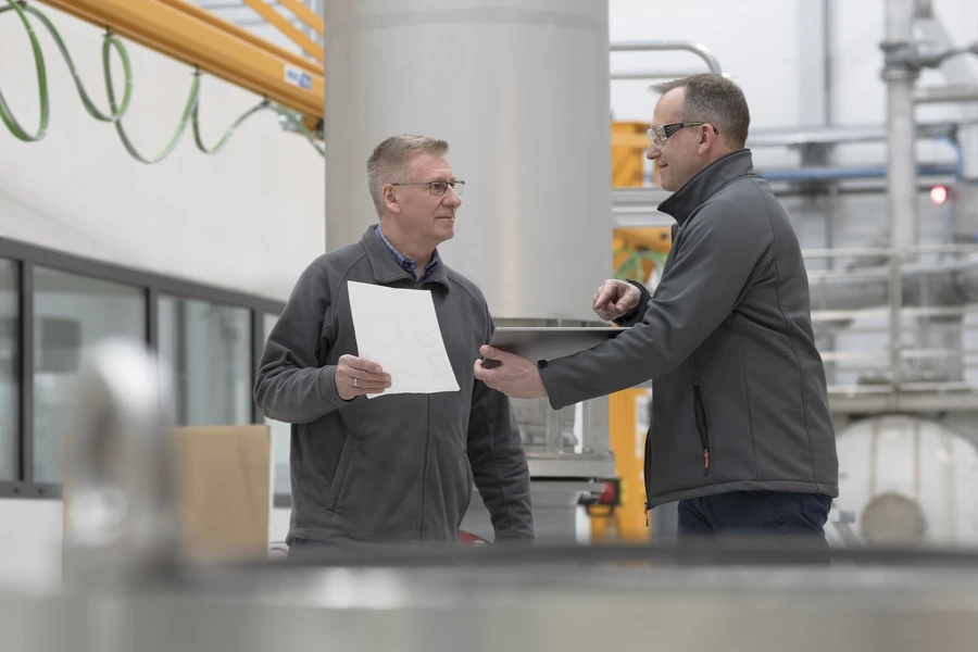 A supervisor discussing a document with an employee in an industrial setting, showcasing expertise at a glance for glossary purposes